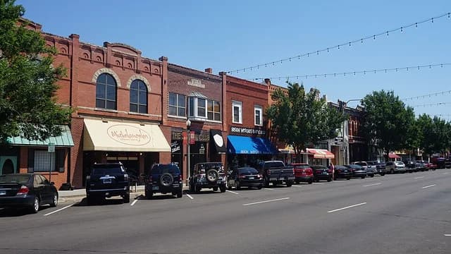 Historic brick storefronts and leafy sidewalks along East Main Street in downtown Norman, Oklahoma