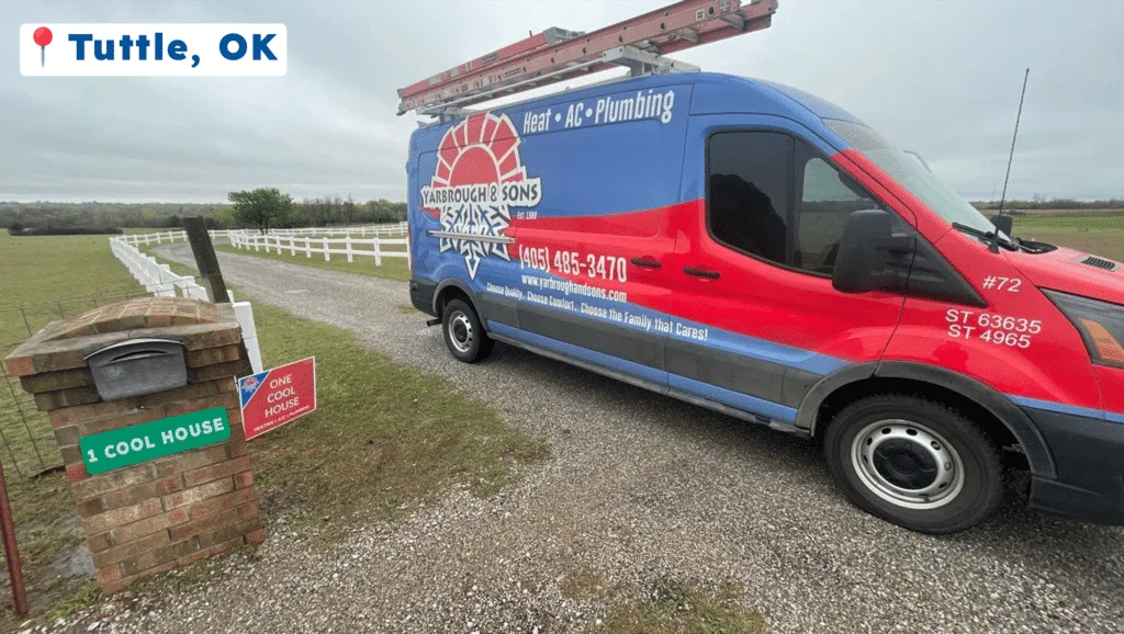 A blue and red plumbing service van parked on gravel near a white fence.