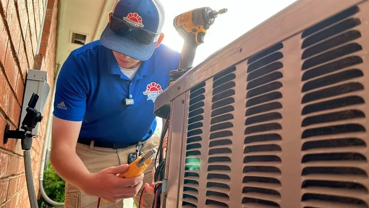 HVAC technician in Quail Creek, OK, performing maintenance on an outdoor air conditioning unit, using a multimeter to check electrical connections.