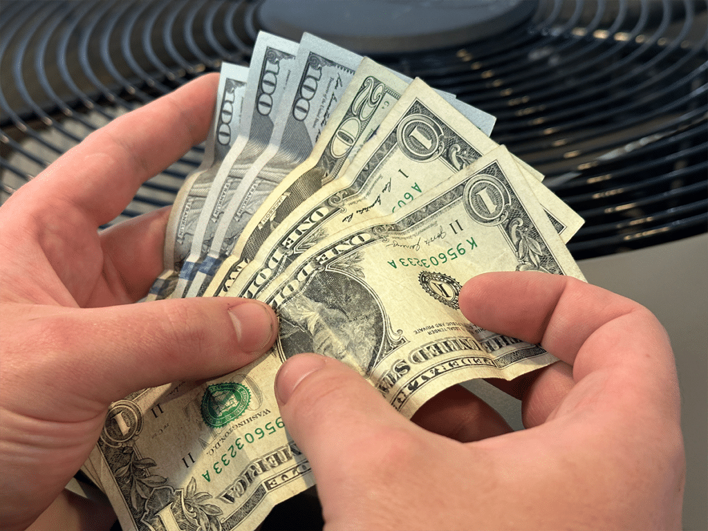 Dollar bills amounting to $322, fanned out between two hands holding the bills over an AC condenser.