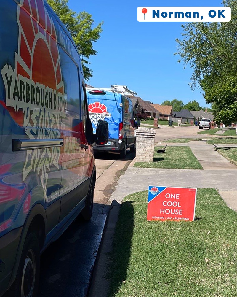 Two Yarbrough & Sons service vans parked at a Norman, OK home, with a βOne Cool Houseβ yard sign displayed on the lawn after completing HVAC maintenance and plumbing upgrades.