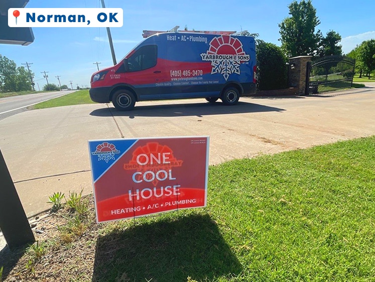 Yarbrough & Sons service van parked in a driveway in Norman, OK, with a red and blue yard sign in the foreground that reads "One Cool House – Heating • A/C • Plumbing."